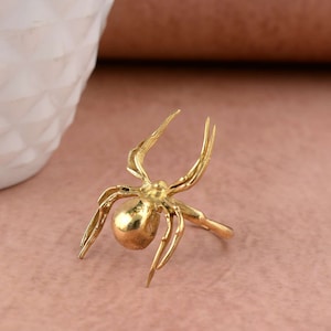 May include: A gold-toned spider ring with a detailed design. The ring is made of metal and has a realistic spider shape.