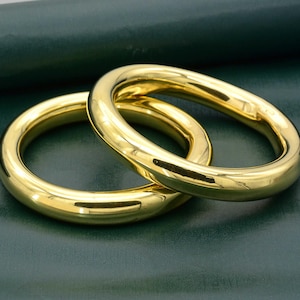 Könnte beinhalten: Zwei glänzende goldene Ringe, einer etwas größer als der andere, liegen übereinander. Die Ringe sind glatt und haben eine polierte Oberfläche.