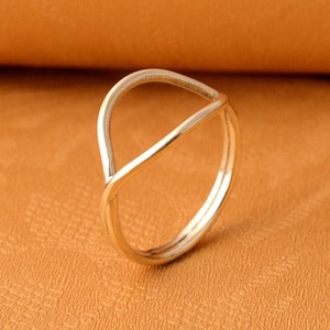 Könnte beinhalten: Ein silberner Ring mit einem einfachen, offenen Design. Der Ring ist aus glattem, poliertem Metall gefertigt und hat eine minimalistische Ästhetik.