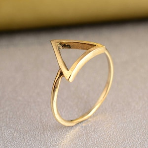 Könnte beinhalten: Ein goldfarbener Ring mit einem dreieckigen Design. Der Ring ist schlicht und minimalistisch.