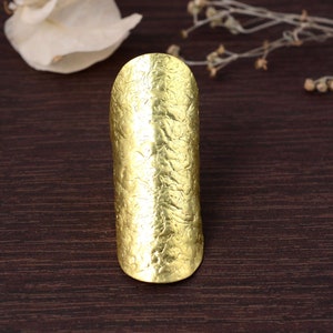 Könnte beinhalten: Ein breiter, goldfarbener Ring mit Textur. Der Ring ist aus Metall und hat eine gehämmerte Oberfläche.