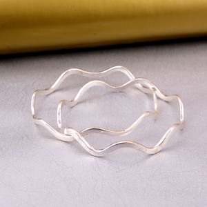 May include: Two silver wavy bangles, stacked on top of each other, on a gray surface.