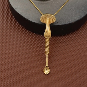 May include: A gold-tone necklace featuring a mushroom-shaped pendant. The pendant has an intricate design and a small spoon at the bottom.