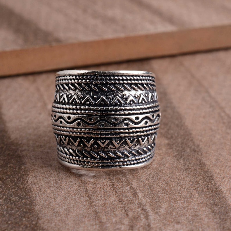 Peut inclure: Une bague en argent avec une large bande orn&eacute;e d'un motif g&eacute;om&eacute;trique complexe. Le design comprend une s&eacute;rie de lignes ondul&eacute;es, de triangles et de points.