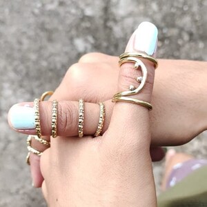 May include: A set of gold-toned rings, including a unique crescent moon design with small beads, worn on a finger.