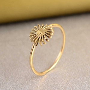 Könnte beinhalten: Ein goldener Ring mit einem zarten, sonnenförmigen Design. Der Ring ist schlicht und elegant, mit einer glatten, polierten Oberfläche.