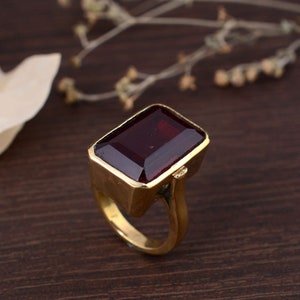 Könnte beinhalten: Ein goldener Ring mit einem großen, rechteckigen, dunkelroten Edelstein.