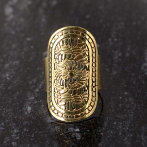 May include: A gold-toned ring with an oval-shaped design featuring intricate floral patterns. The ring is made of metal and has a smooth, polished finish.