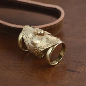 May include: Gold-toned adjustable ring with a flower design and a small, round stone in the center. The ring is made of metal and has a textured finish.