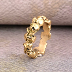 Könnte beinhalten: Ein goldfarbener Ring mit einer Reihe von Totenköpfen. Die Totenköpfe sind detailliert und haben einen leicht gealterten Look.