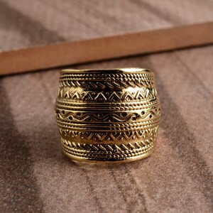 Peut inclure: Une bague en m&eacute;tal dor&eacute; avec une large bande orn&eacute;e d'un motif g&eacute;om&eacute;trique complexe. La bague est en m&eacute;tal et a une finition polie.
