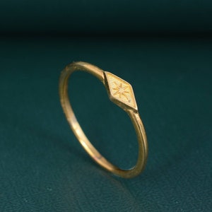 Könnte beinhalten: Ein goldener Ring mit einem rautenförmigen Design, das einen Stern in der Mitte zeigt.