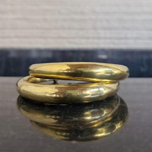 Könnte beinhalten: Zwei goldene Creolen, die übereinander liegen. Die Ohrringe sind dick und haben eine glatte, polierte Oberfläche.