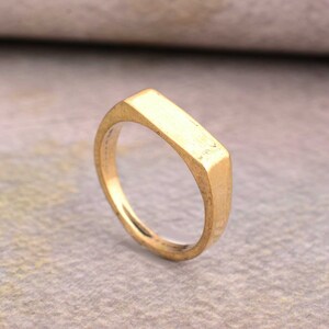 Könnte beinhalten: Ein goldfarbener Ring mit einem flachen, rechteckigen Band.