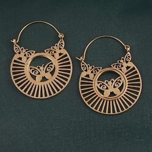 May include: A pair of gold-toned hoop earrings with a delicate butterfly design. The earrings feature a circular shape with a sunburst pattern and a smaller butterfly cutout in the centre.