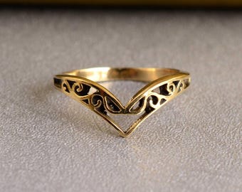 May include: A gold-colored ring with a delicate, openwork design in the shape of a V. The ring is made of metal and has a smooth, polished finish.