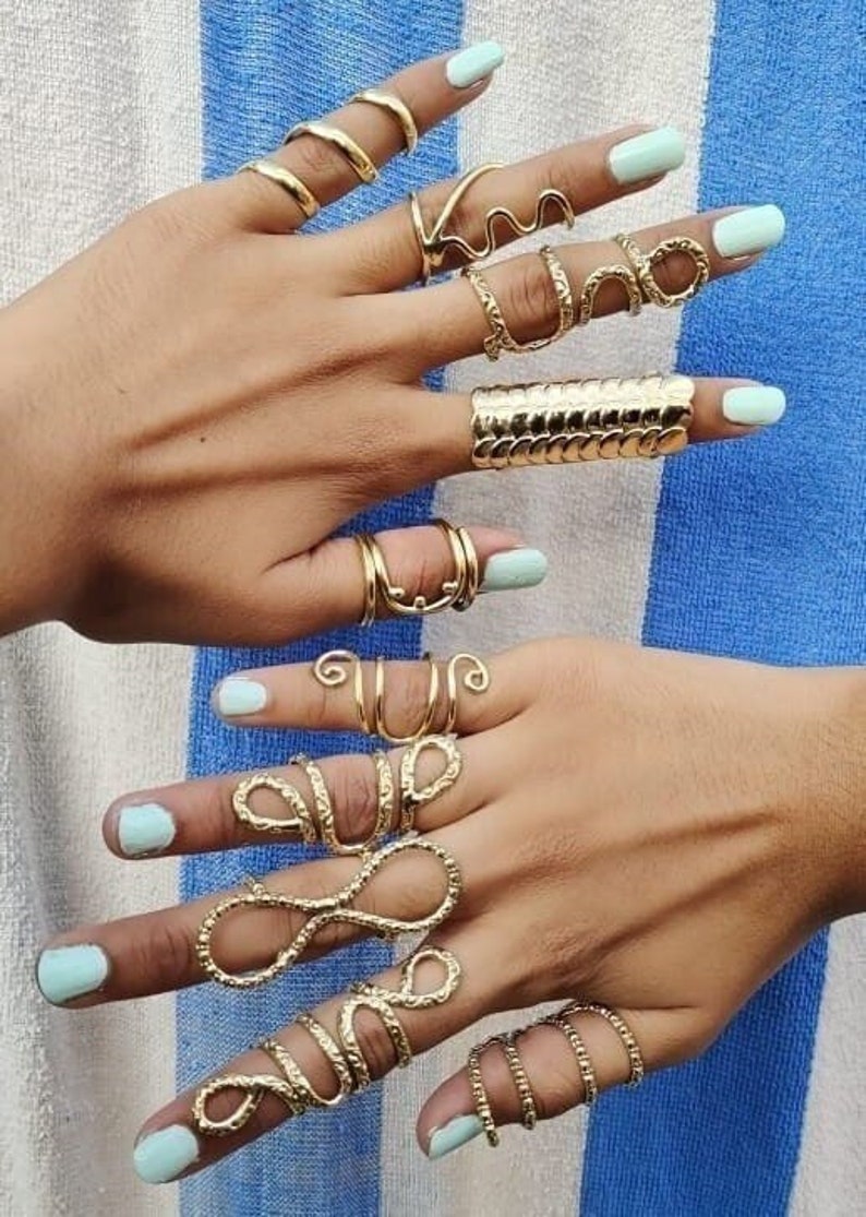 May include: A set of gold-toned rings with various designs, including a snake, a wave, and a geometric pattern. The rings are worn on multiple fingers.