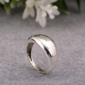 Könnte beinhalten: Ein silberner Ring mit abgerundeter, gewölbter Oberseite. Der Ring ist glatt und glänzend.