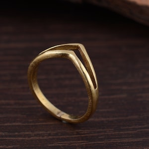 Könnte beinhalten: Ein goldfarbener Ring mit einem einzigartigen V-förmigen Design. Der Ring ist aus Metall und hat eine glatte, polierte Oberfläche.