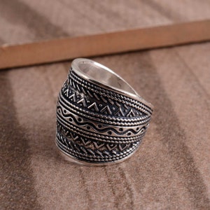 Peut inclure: Une bague en argent avec une large bande orn&eacute;e d'un motif g&eacute;om&eacute;trique complexe. Le design comprend une s&eacute;rie de triangles r&eacute;p&eacute;t&eacute;s, de lignes ondul&eacute;es et de points.