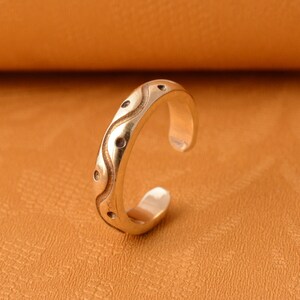 Può includere: Un anello d'argento con un design ondulato e piccoli punti. L'anello è regolabile e aperto.