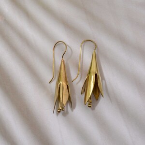 Könnte beinhalten: Ein Paar goldfarbene Ohrringe in Form von zarten Blüten. Die Ohrringe haben ein schlichtes, elegantes Design.