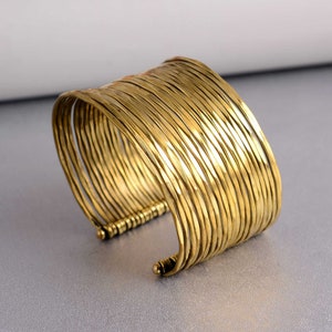 May include: A gold-toned metal cuff bracelet made of multiple thin, hammered bands. The bracelet is open and adjustable.