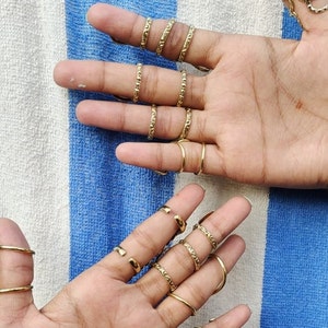 May include: A set of gold-toned rings with a textured design. The rings are worn on multiple fingers of both hands.
