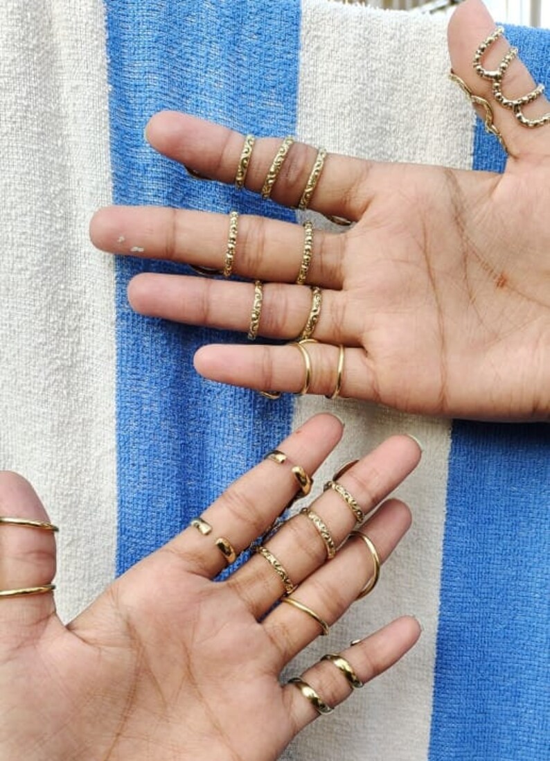 May include: A set of gold-toned rings with a textured design. The rings are worn on multiple fingers of both hands.