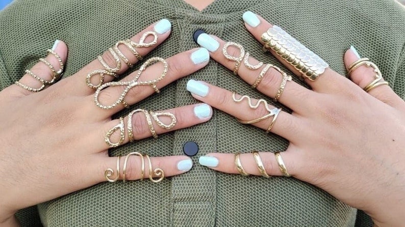 May include: A set of gold-toned rings with various designs, including a snake, a wave, and an infinity symbol. The rings are worn on multiple fingers.
