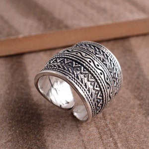 Peut inclure: Bague en argent avec une large bande orn&eacute;e d'un motif g&eacute;om&eacute;trique complexe. Le motif est compos&eacute; de triangles, de lignes ondul&eacute;es et de points r&eacute;p&eacute;t&eacute;s.