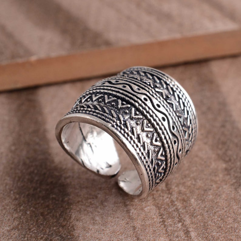 Peut inclure: Bague en argent avec une large bande orn&eacute;e d'un motif g&eacute;om&eacute;trique complexe. Le motif est compos&eacute; de triangles, de lignes ondul&eacute;es et de points r&eacute;p&eacute;t&eacute;s.