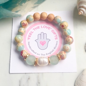 May include: A turquoise and brown stone bracelet with gold accents and a white pearl. The bracelet is on a white card with the text "'Feel The Love' Gifts Handcrafted on The English Riviera".