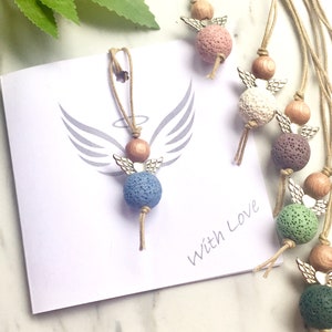 May include: A set of six angel-shaped lava stone diffusers with wooden beads and silver wings. The diffusers are in various colours, including pink, white, purple, green, and blue. The diffusers are strung on twine and come with a card that says "With Love".
