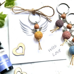 May include: A set of four angel keychains with lava rock beads and wooden accents. The keychains are tied together with twine and have a handwritten note that says "With Love".