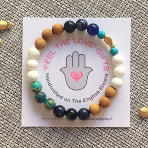 May include: A bracelet with blue, white, brown, and turquoise beads, a gold fish charm, and the text "'Feel The Love' Gifts The English Riviera".