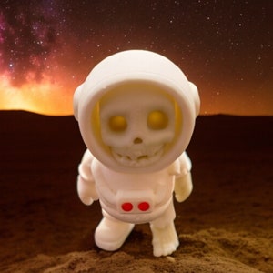 May include: White astronaut figurine with a skull face, standing on a brown surface with a starry night sky background.