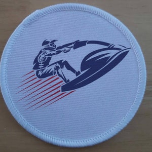 May include: White round patch with a blue and white illustration of a person riding a jet ski. The jet ski is leaving a red and white wake behind it.