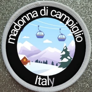May include: A white and black circular patch with the text "Madonna di Campiglio Italy" and a cartoon image of a snowy mountain scene with ski lifts and a small cabin.