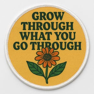 May include: Circular patch featuring the text "GROW THROUGH WHAT YOU GO THROUGH" in dark green. The patch has a yellow background with an orange flower and green leaves. It is edged with white stitching.
