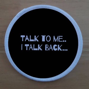 Peut inclure: Un écusson rond noir avec le texte brodé blanc "TALK TO ME... I TALK BACK...". Le patch a une bordure blanche cousue.