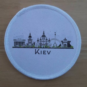 May include: White round fabric patch with a black and white cityscape of Kiev, Ukraine. The text "KIEV" is printed below the cityscape.