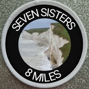 May include: A black and white round patch with the text "SEVEN SISTERS 8 MILES" and a photo of white cliffs and a blue sea.