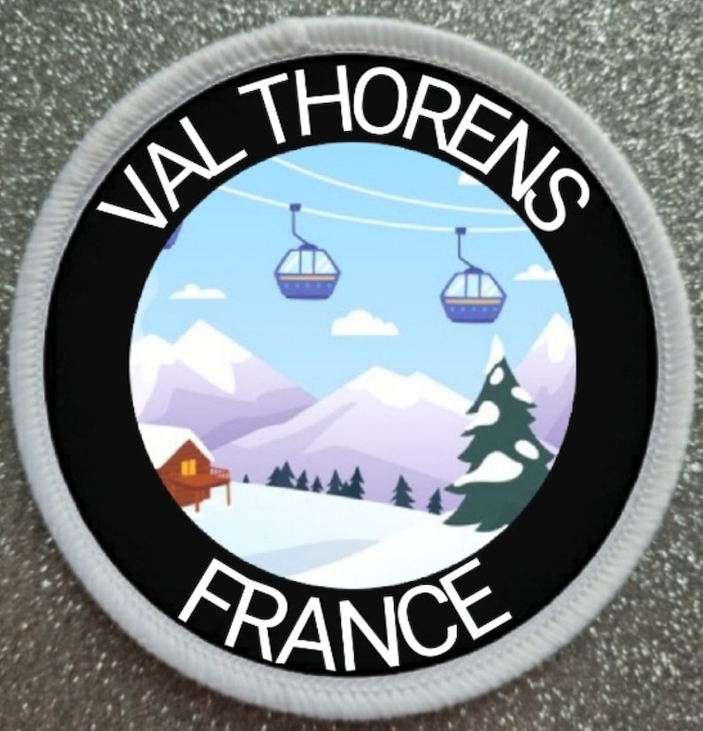 K&ouml;nnte beinhalten: Ein wei&szlig;er und schwarzer runder Patch mit dem Text "Val Thorens France" und einem Cartoon-Bild einer verschneiten Berglandschaft mit Skiliften und einer kleinen H&uuml;tte.