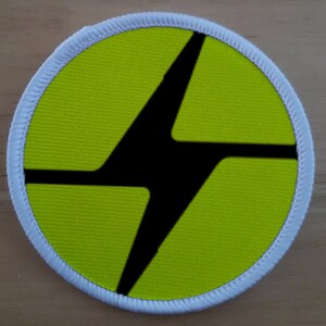 May include: A round, yellow patch with a black lightning bolt design. The patch has a white border.