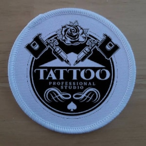 May include: White round patch with black and white design. The design features two crossed tattoo machines, a rose, and the text "TATTOO PROFESSIONAL STUDIO".