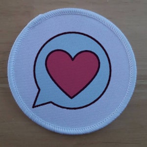 Può includere: Toppa rotonda in tessuto bianco con un fumetto blu che contiene un cuore rosa.