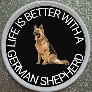 May include: A black and white round patch with a white border. The patch features a German Shepherd dog sitting on a black background. The text on the patch reads "Life is better with a German Shepherd".