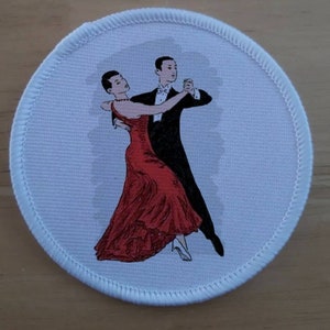 May include: Round white patch with a stitched border featuring a couple dancing. The woman wears a red dress, and the man is in a black tuxedo. The illustration depicts a classic ballroom dance pose.