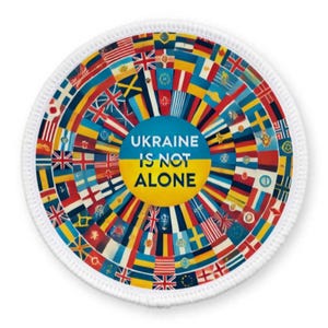 May include: A white circular patch with a colorful design of flags from around the world. The center of the patch features a blue and yellow circle with the text "UKRAINE IS NOT ALONE" in white.